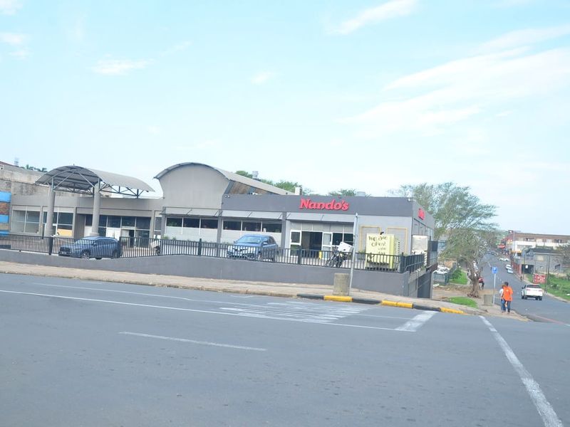 Street-level view of a commercial property featuring a modern curved roof design, perimeter fencing, and prominent signage along a main road.