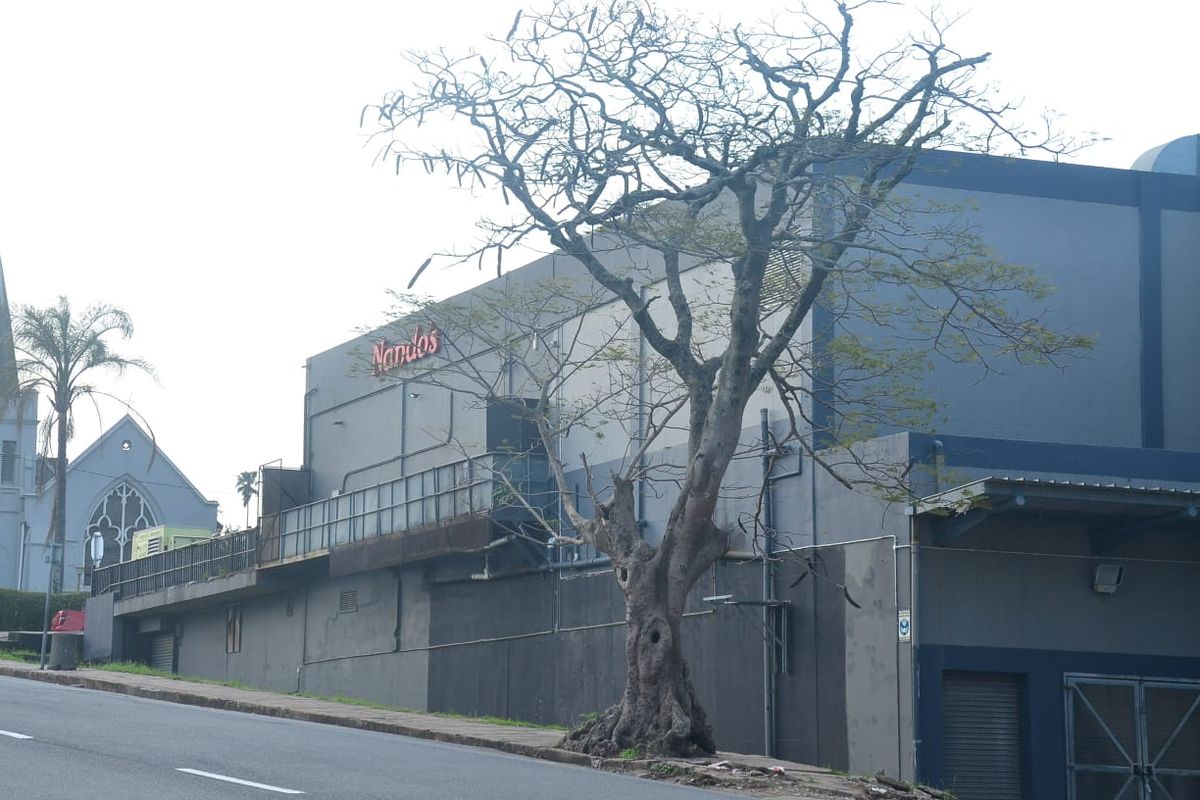 Street-level view of a commercial building facade featuring prominent signage, metal security railings, and roller shutters.