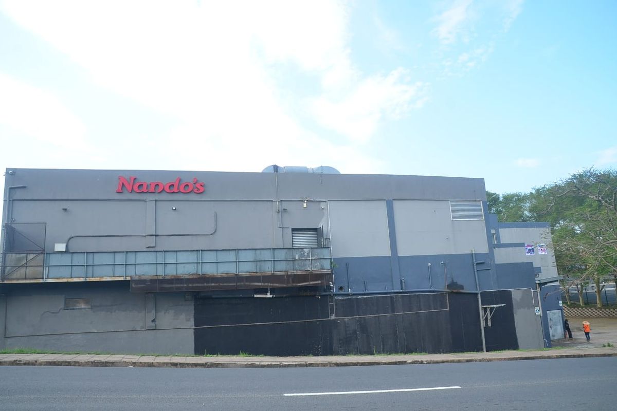 Exterior view of a commercial building facade featuring prominent signage, metal railings, and ventilation infrastructure along a street frontage.