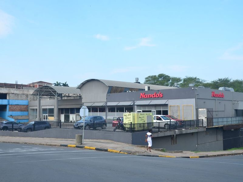 Exterior view of a commercial building featuring a Nando's restaurant, associated parking area, and metal structural elements.