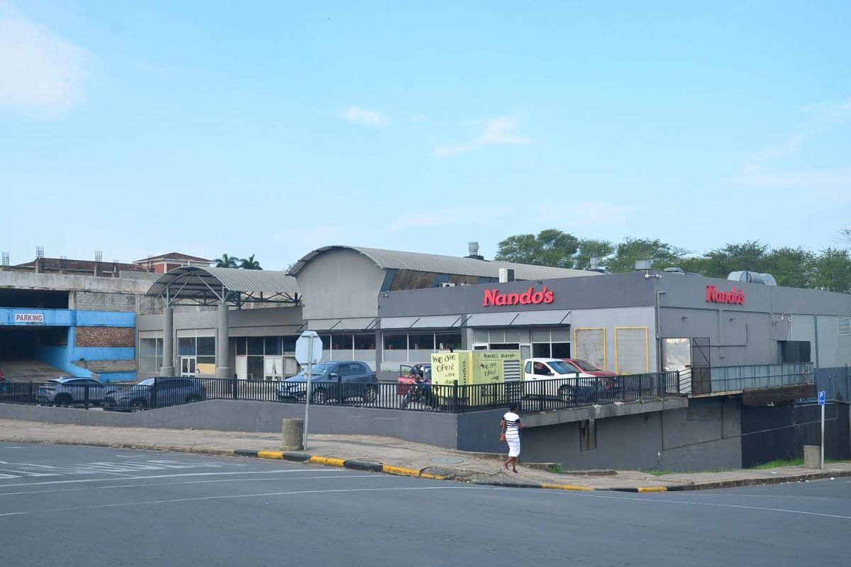Exterior view of a commercial building featuring a Nando's restaurant, associated parking area, and metal structural elements.
