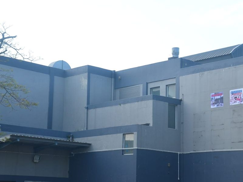 Rear exterior view of a commercial building featuring painted concrete walls, roof ventilation, and an awning over a service entrance area.