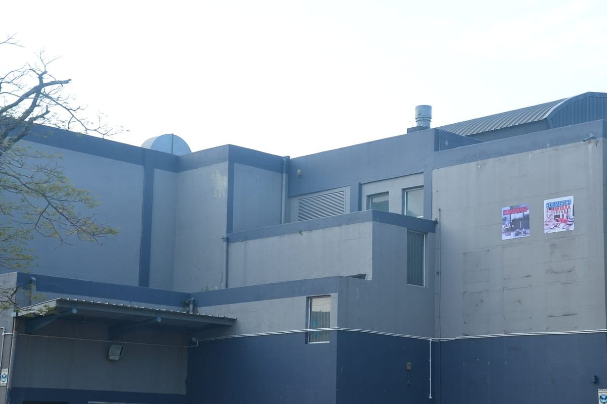 Rear exterior view of a commercial building featuring painted concrete walls, roof ventilation, and an awning over a service entrance area.