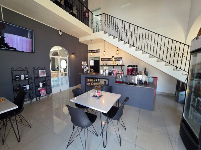 Open plan retail space featuring a service counter, tiled flooring, and a prominent staircase with decorative wrought iron railing.