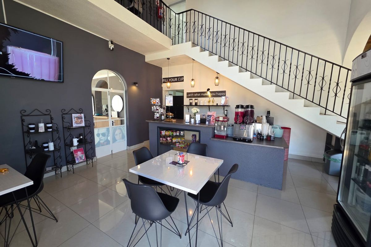 Open plan retail space featuring a service counter, tiled flooring, and a prominent staircase with decorative wrought iron railing.