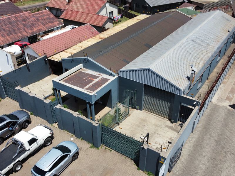 Aerial view of an industrial property featuring a corrugated metal roof, secure perimeter wall with electric fencing, and a roller shutter door access point.