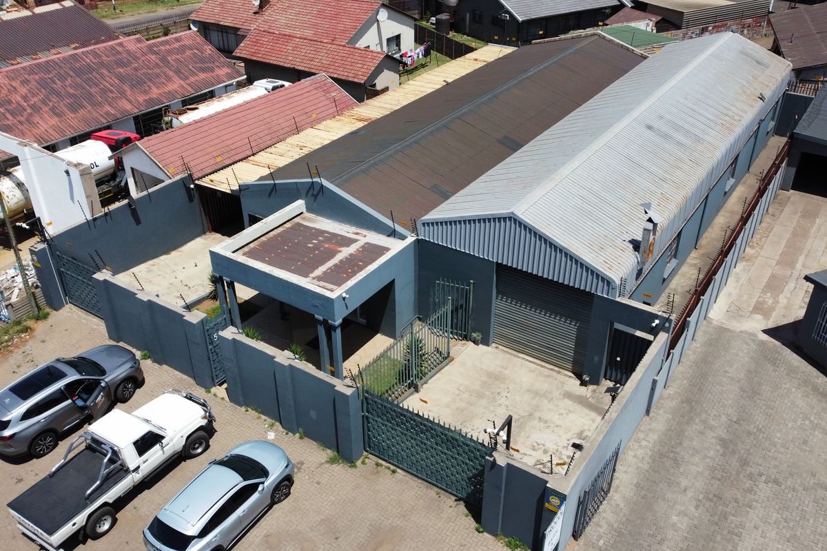 Aerial view of an industrial property featuring a corrugated metal roof, secure perimeter wall with electric fencing, and a roller shutter door access point.