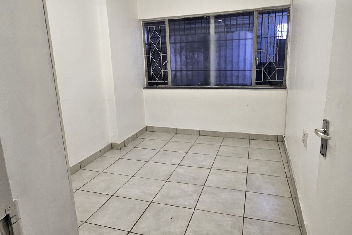 An empty bedroom featuring tiled flooring and a window fitted with security bars, offering a clean and functional space ready for customization.