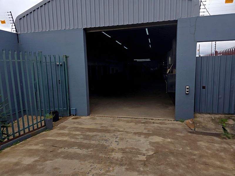 Front view of an industrial warehouse featuring a large roller shutter entrance, concrete driveway, and secure perimeter fencing with electric security wires.