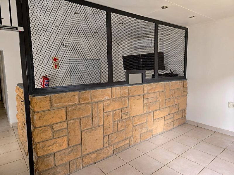 Industrial office space featuring a stone-clad partition wall with a metal mesh security screen, tiled flooring, and integrated air conditioning.