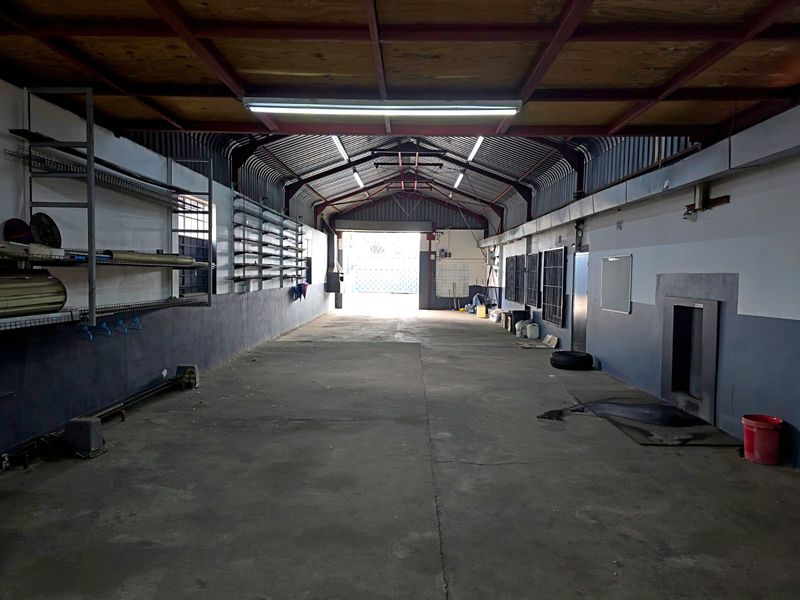 Spacious industrial utility area featuring exposed steel roof trusses, corrugated metal ceiling, concrete flooring, and wall-mounted metal shelving units.