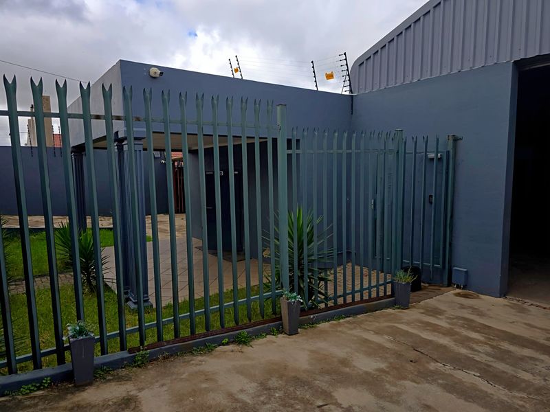 Industrial property exterior featuring secure steel palisade fencing with electric security, paved driveway access, and a covered entrance area.