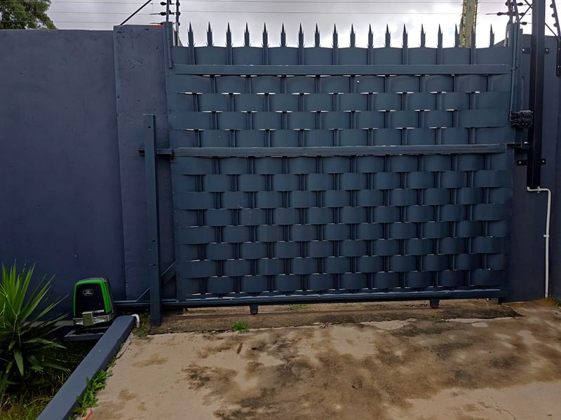 Secure industrial property entrance featuring a modern dark grey woven-style sliding gate with integrated electric fencing and automated gate motor.