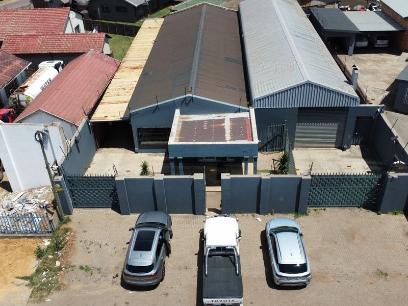 Aerial view of an industrial property featuring a corrugated metal roof, secure perimeter wall with electric fencing, and a paved driveway.
