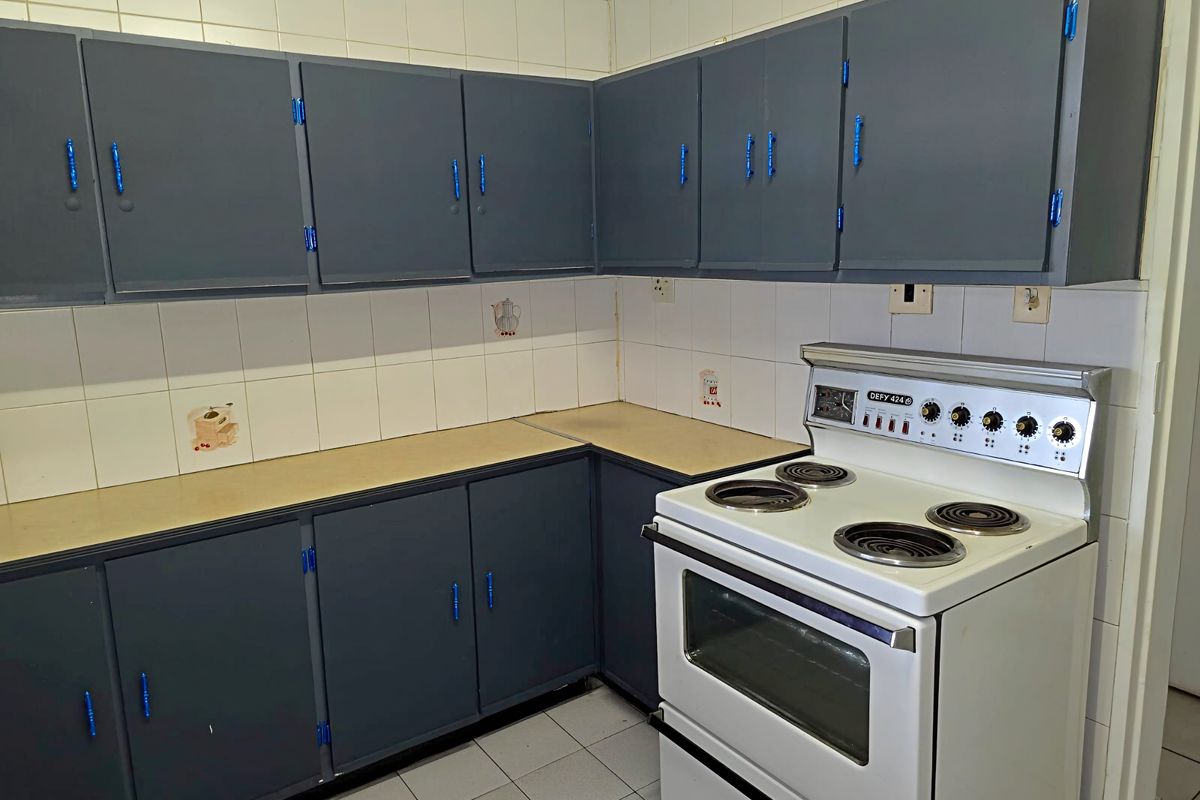 A functional kitchen space featuring built-in cabinetry, laminate countertops, and a freestanding electric stove with oven, finished with ceramic wall and floor tiles.