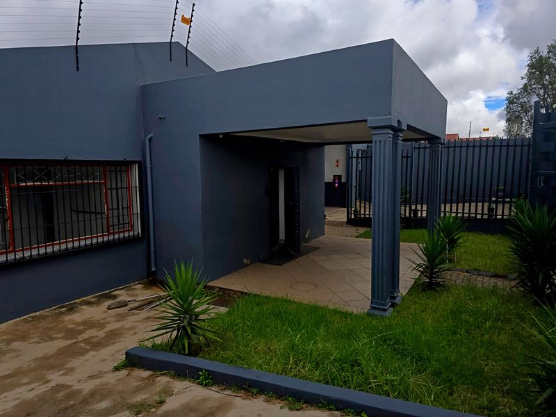 Front entrance area of an industrial property featuring a covered porch, security fencing, and security bars on windows.