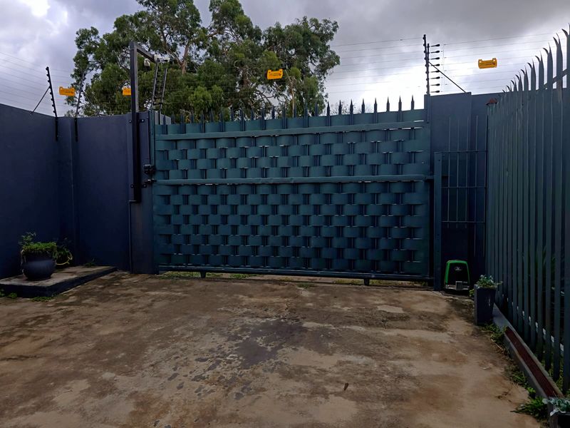 Secure industrial property entrance featuring a heavy-duty electric sliding gate, perimeter wall with electric fencing, and a concrete driveway.