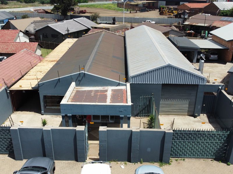 Aerial view of an industrial property featuring dual warehouse structures with corrugated metal roofing, secure perimeter walling, and electric fencing.