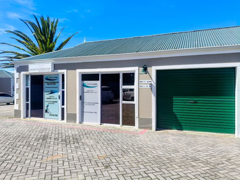 Front facade of a commercial property featuring a paved driveway, roller shutter garage door, and glass entrance doors with signage.