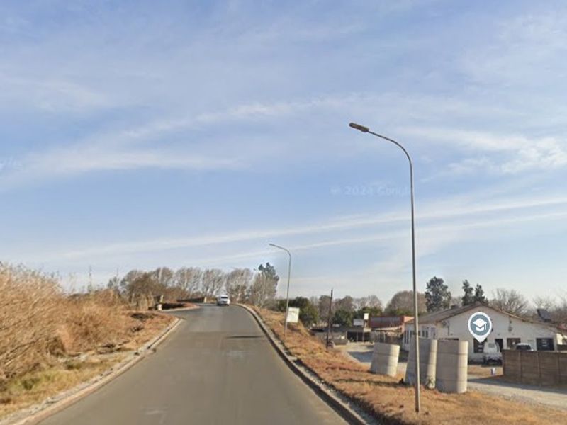 A street view showing the approach to the industrial property with asphalt road access, street lighting, and perimeter boundary walling.