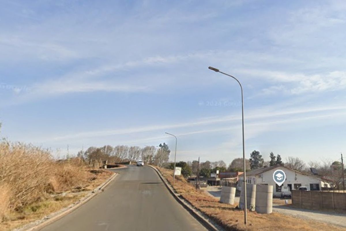 A street view showing the approach to the industrial property with asphalt road access, street lighting, and perimeter boundary walling.