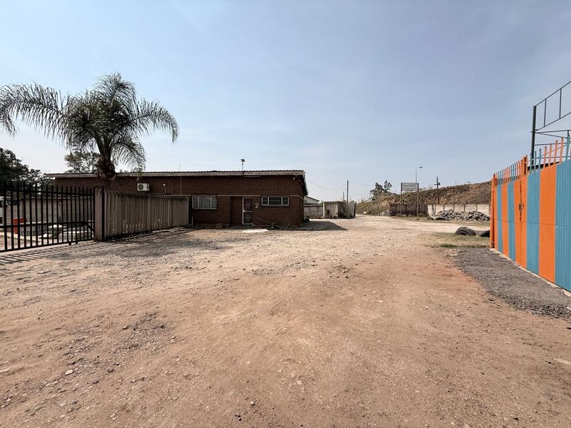 Front exterior view of an industrial property featuring a brick building, security fencing, and an unpaved yard area.
