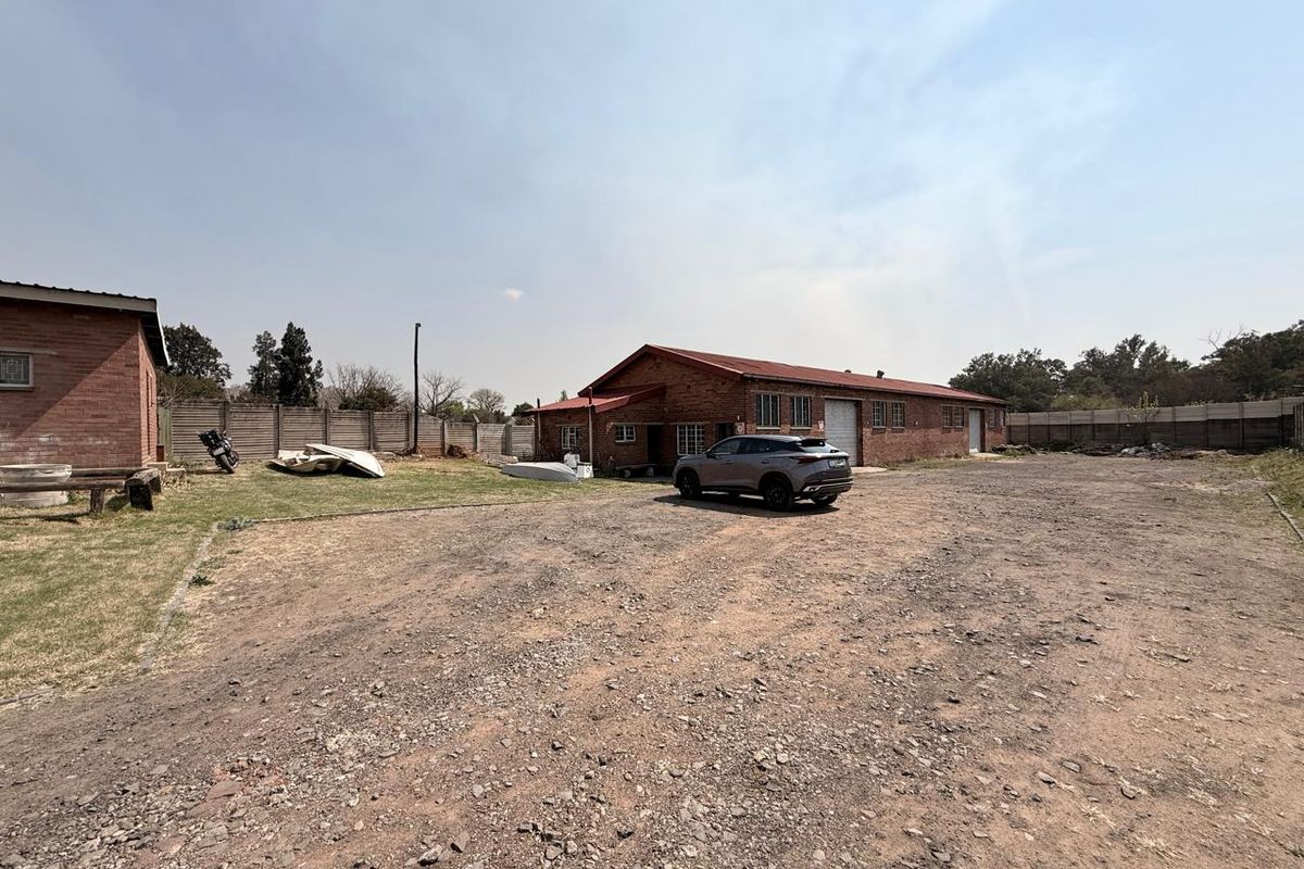 Spacious industrial property exterior featuring a large gravel yard, brick buildings with metal roofing, and secure perimeter walling.