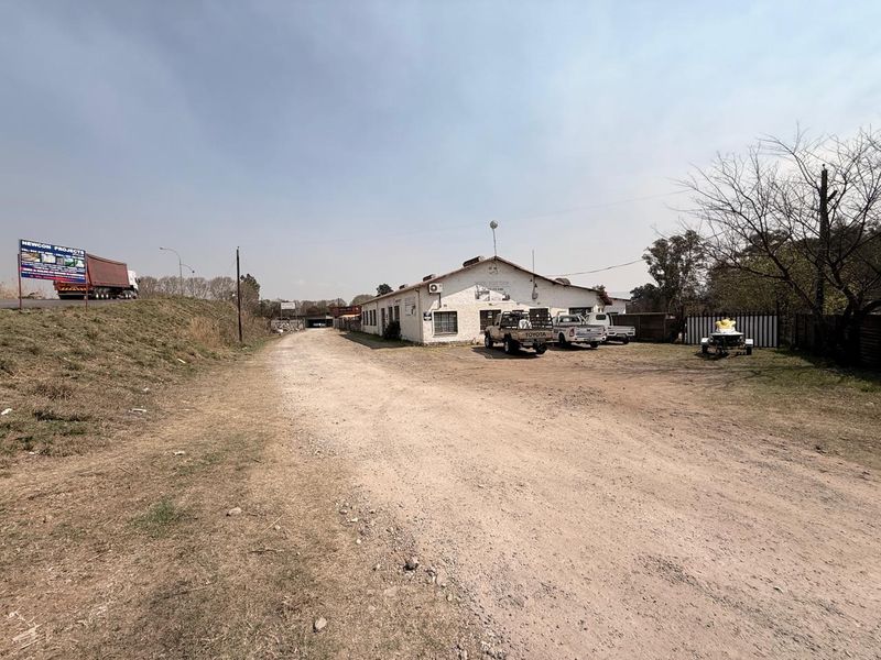 Exterior view of an industrial property featuring a large unpaved yard area and a single-story building with external air conditioning units.