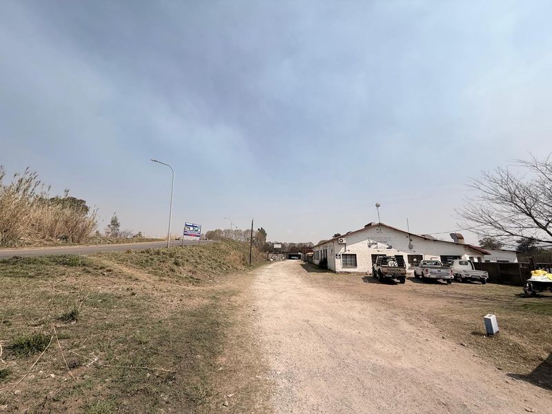 Exterior view of an industrial property featuring a gravel driveway and a single-story building with external air conditioning units.