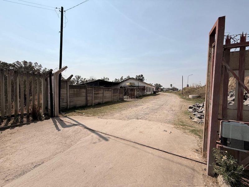 Industrial property entrance featuring a concrete driveway, secure steel gate, and perimeter precast concrete walling with barbed wire security.