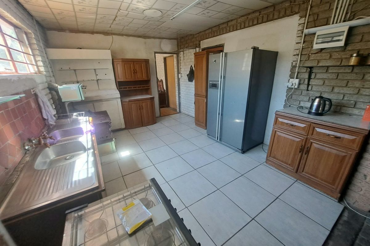 A dated kitchen featuring exposed brick walls, tiled flooring, and built-in wooden cabinetry, offering significant potential for modernization and renovation.