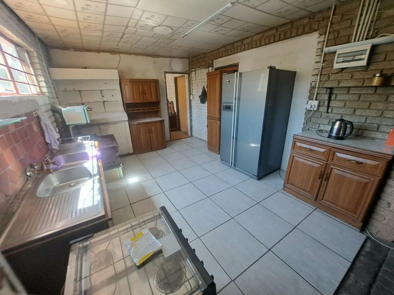A dated kitchen featuring exposed brick walls, tiled flooring, and built-in wooden cabinetry, offering significant potential for modernization and renovation.