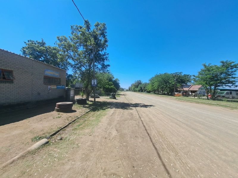 A street view showing an unpaved road adjacent to a brick building structure in a rural or semi-industrial setting.