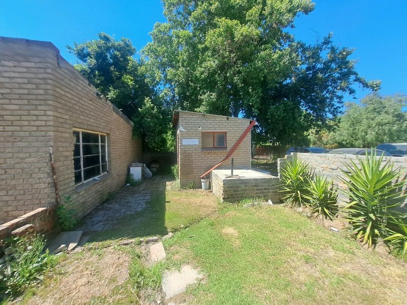 Rear exterior view of the office property featuring brick outbuildings, a paved walkway, and a small garden area with stone boundary walls.