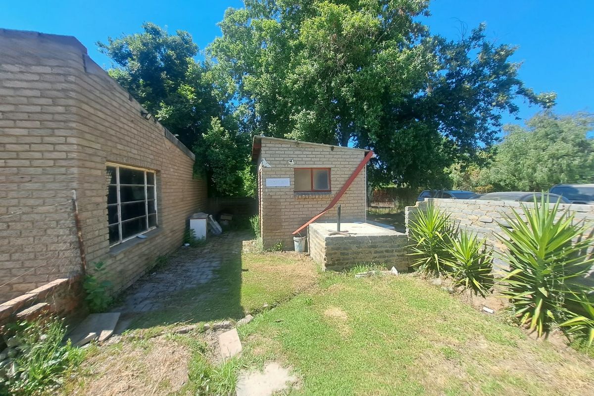 Rear exterior view of the office property featuring brick outbuildings, a paved walkway, and a small garden area with stone boundary walls.
