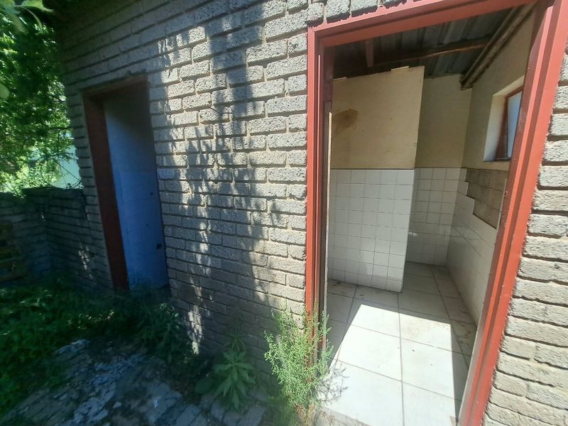 Exterior view of an outdoor utility or restroom structure featuring exposed brick walls, tiled flooring, and visible wear on the finishes.