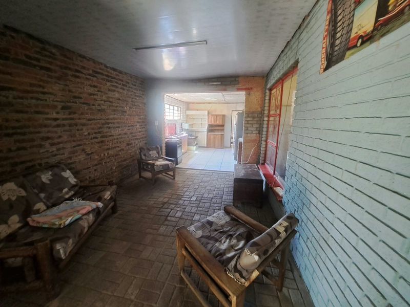 A rustic covered patio area featuring exposed brick walls and paved flooring, providing a transition space leading into the kitchen area.