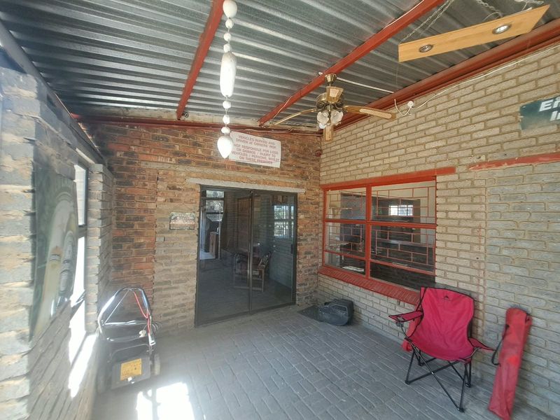 A covered outdoor patio area featuring exposed brick walls, paved flooring, and a corrugated metal roof, providing a functional transition space.