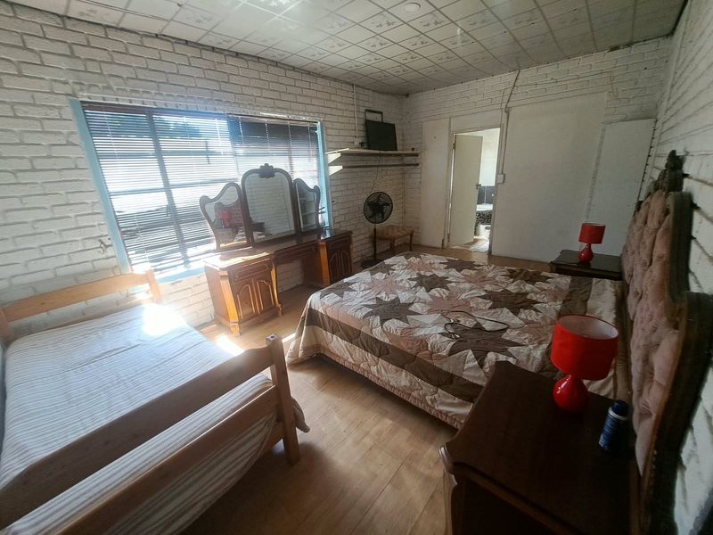 A bedroom featuring exposed brick walls, laminate flooring, and a drop ceiling, with an adjoining doorway leading to a bathroom area.