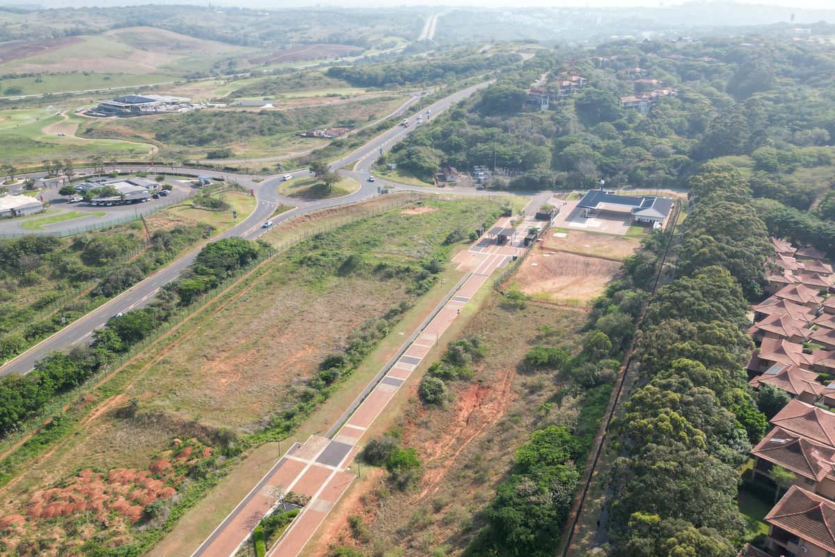 Aerial view of a commercial vacant land plot featuring a paved access road, security gatehouse, and established perimeter fencing in a developed area.