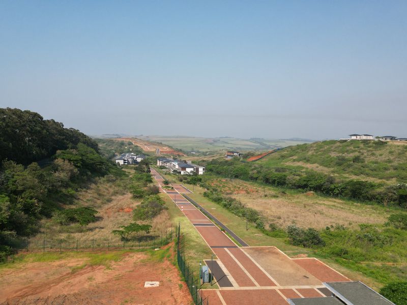 An aerial view of a commercial vacant land development featuring paved walkways, established landscaping, and surrounding natural terrain.