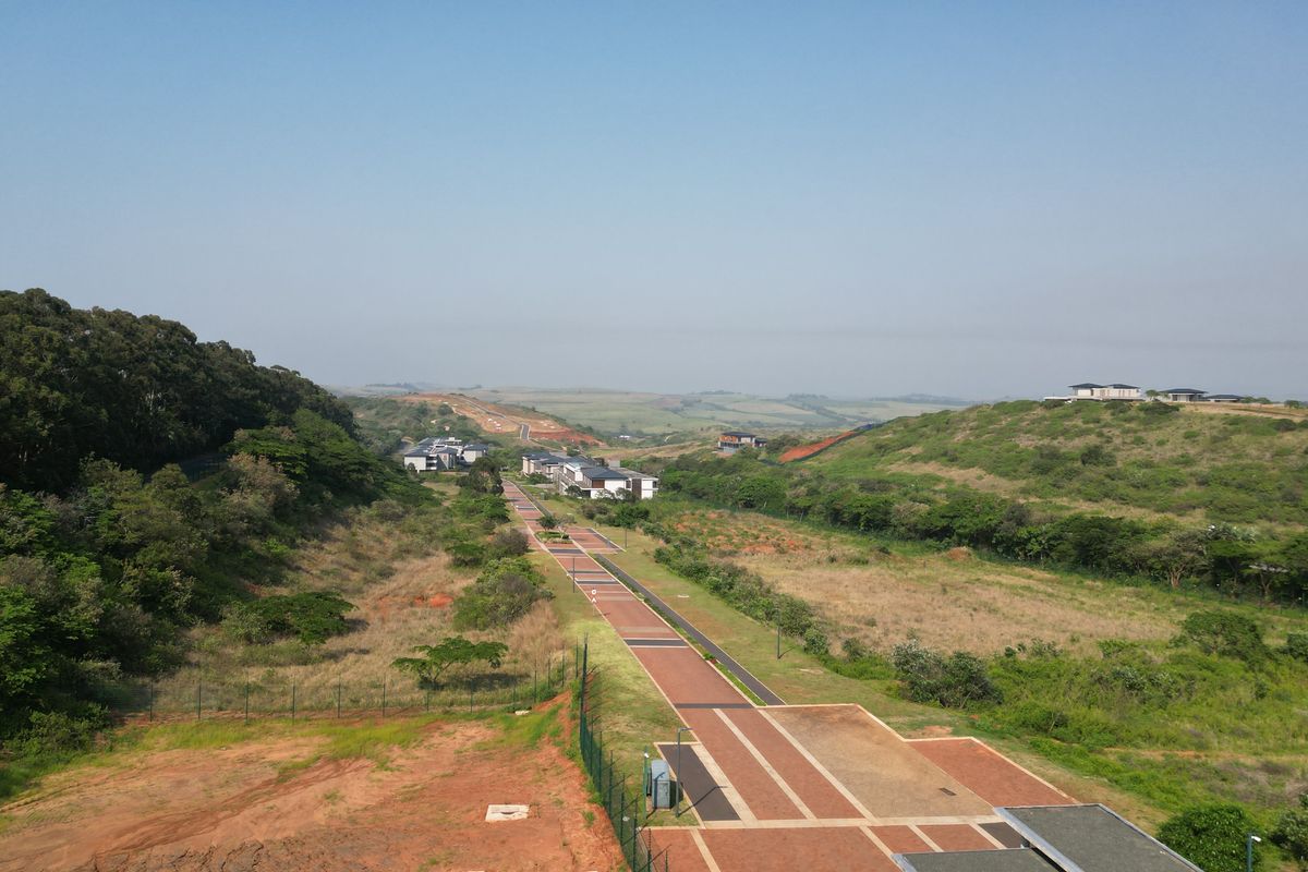 An aerial view of a commercial vacant land development featuring paved walkways, established landscaping, and surrounding natural terrain.