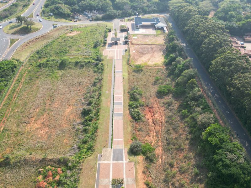 Aerial view of a commercial vacant land plot featuring a central paved walkway, adjacent fuel station infrastructure, and established road access.