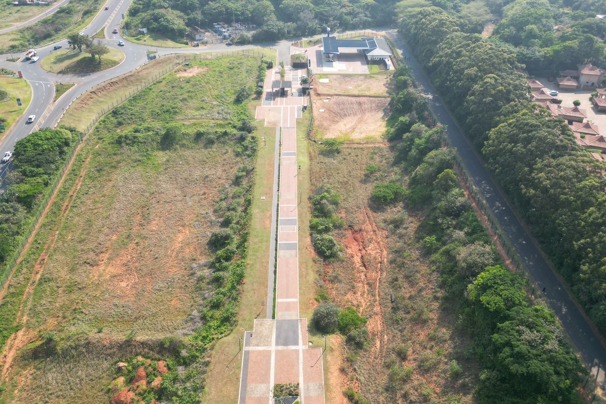 Aerial view of a commercial vacant land plot featuring a central paved walkway, adjacent fuel station infrastructure, and established road access.