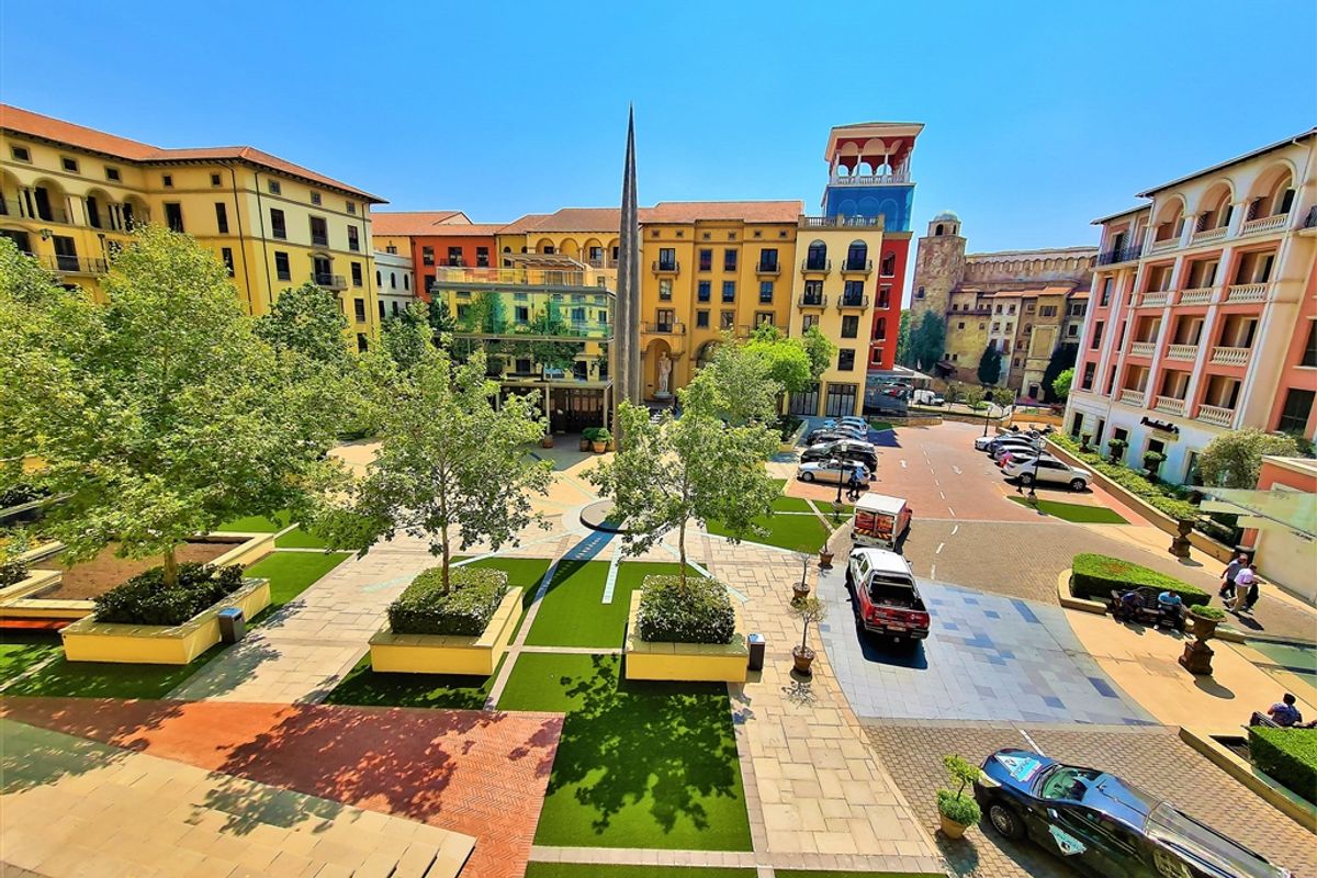 An elevated view of a well-maintained Mediterranean-style office complex courtyard featuring paved walkways, landscaped planters, and a central monument.