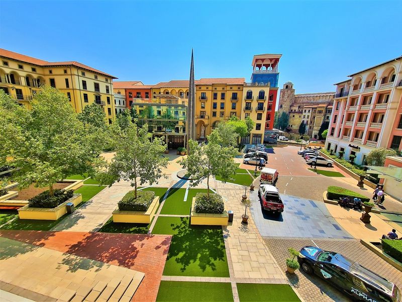An elevated view of a well-maintained Mediterranean-style office complex courtyard featuring paved walkways, landscaped planters, and a central monument.