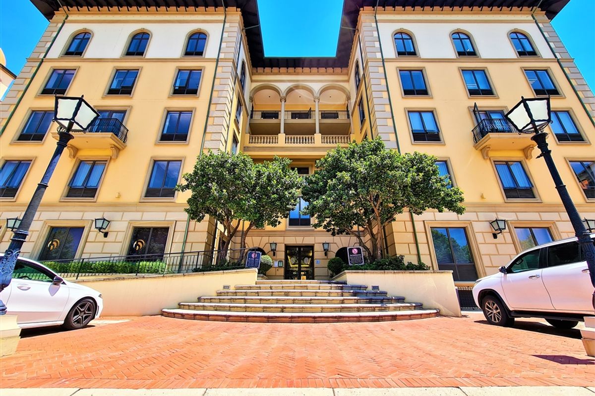 A well-maintained multi-story office building facade featuring classic architectural details, arched windows, wrought iron balconies, and a grand brick-paved entrance with stone steps.