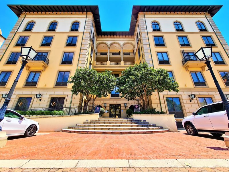 A well-maintained multi-story office building facade featuring classic architectural details, arched windows, wrought iron balconies, and a grand brick-paved entrance with stone steps.