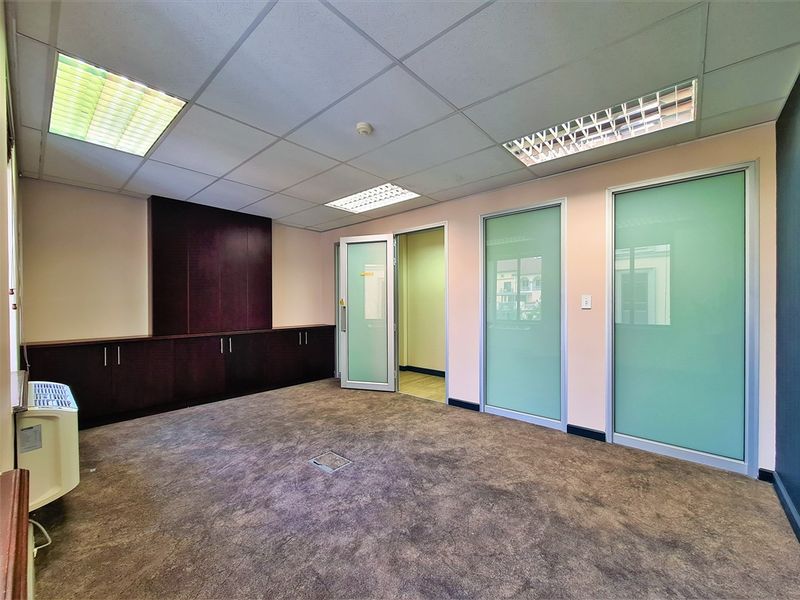 A vacant office space featuring a suspended ceiling, recessed lighting, built-in dark wood cabinetry, and frosted glass partition doors.
