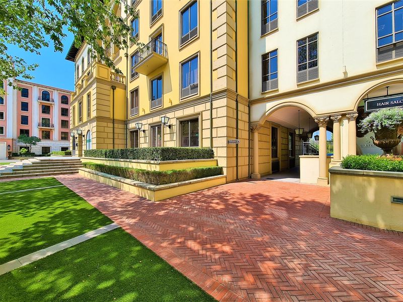 A well-maintained office building exterior featuring classic architectural details, brick paving, landscaped garden beds, and a covered entrance archway.